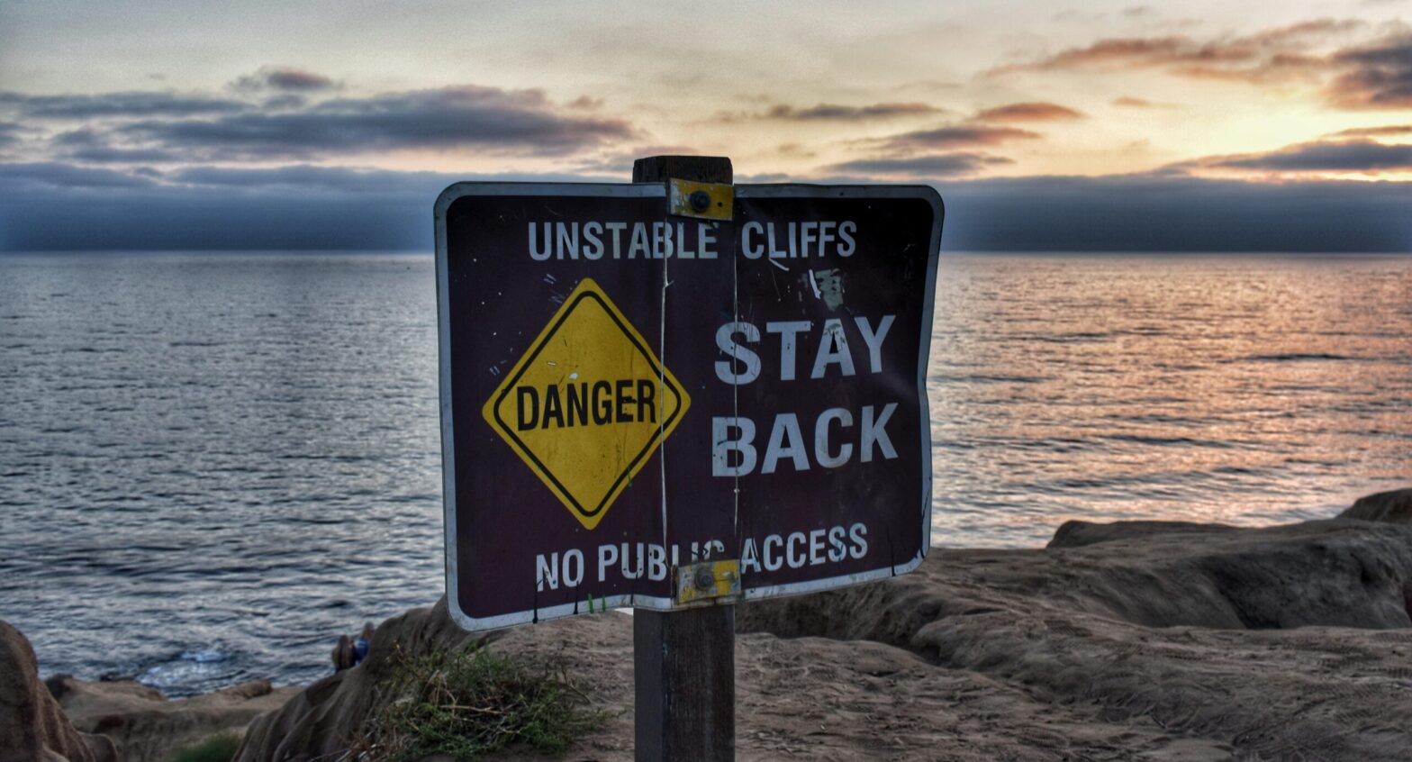 Danger sign warning about unstable cliffs near dangerous rocky coastnear the coast